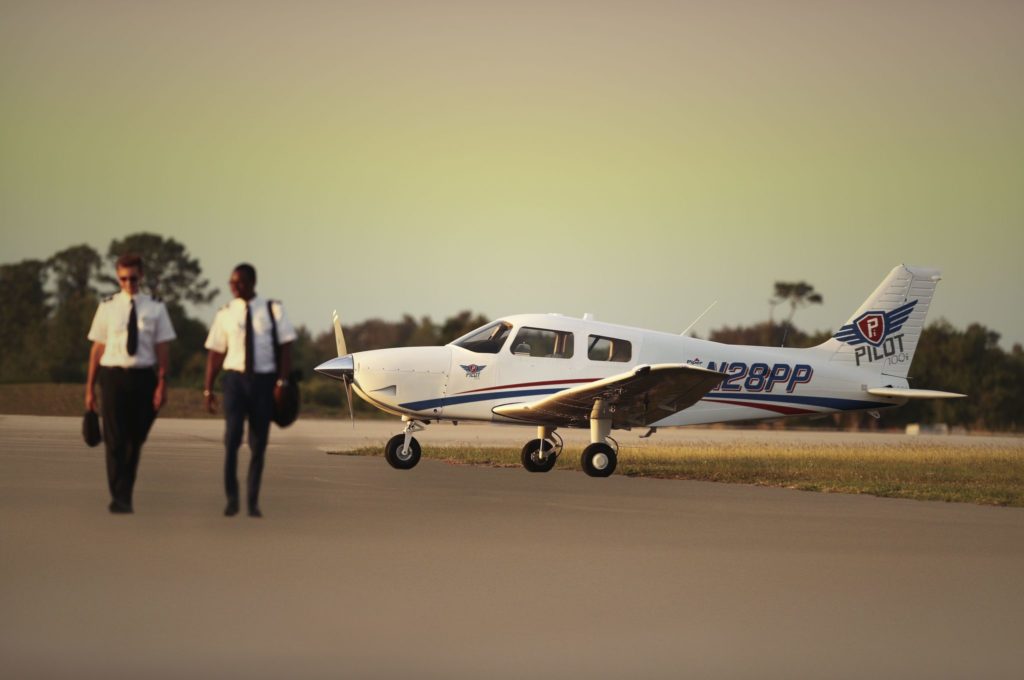 Two pilots walking on the runway next to the Piper Pilot 100i aircraft