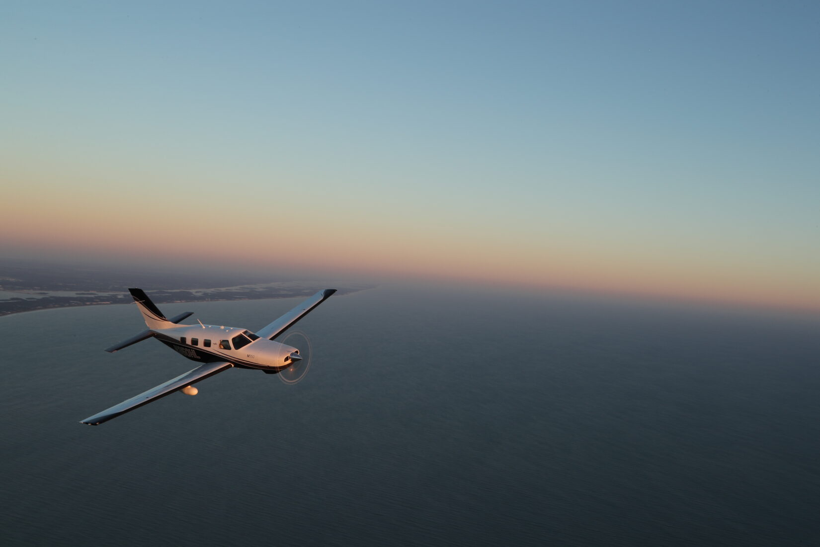 Piper M350 flying over coastline at sunset