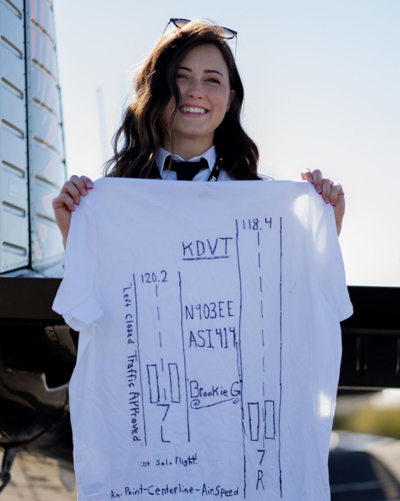 A smiling woman holding a shirt with a design on it