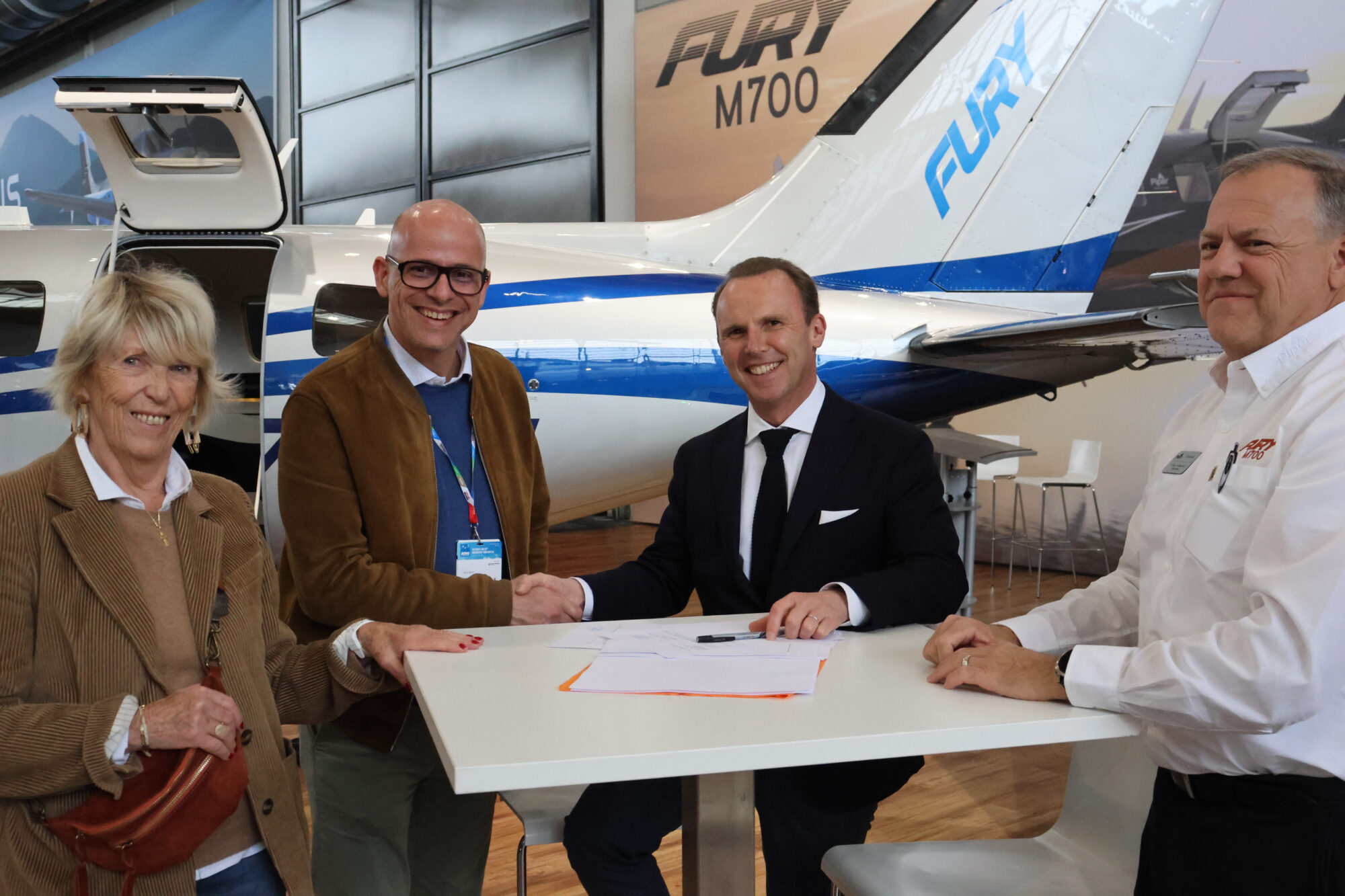 Four people discussing plans at a table with a plane in the background.