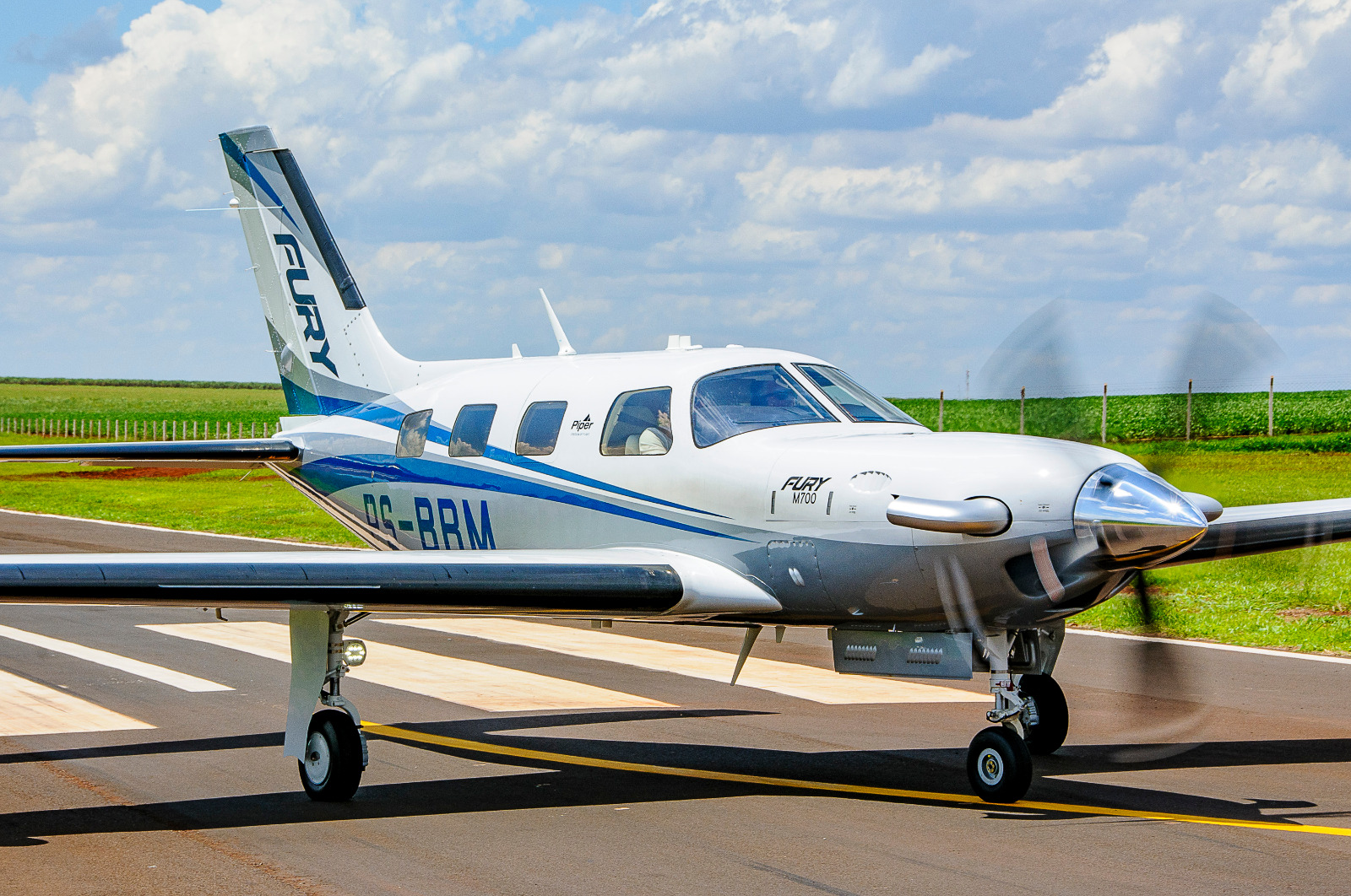 Blogs & Guides 1 Side view of a Piper M700 Fury taxiing on a runway with propeller spinning and green fields in the background.