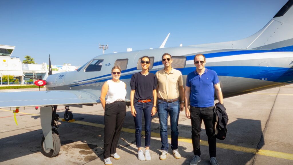 Four Piper European Fly-In attendees stand in front of a blue-and-silver Piper M700 Fury at Portorož Airport.
